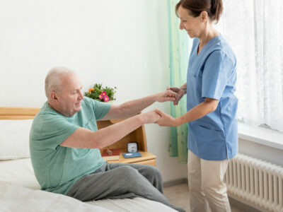 Nursing home – home caregiver helping an elderly man out of bed